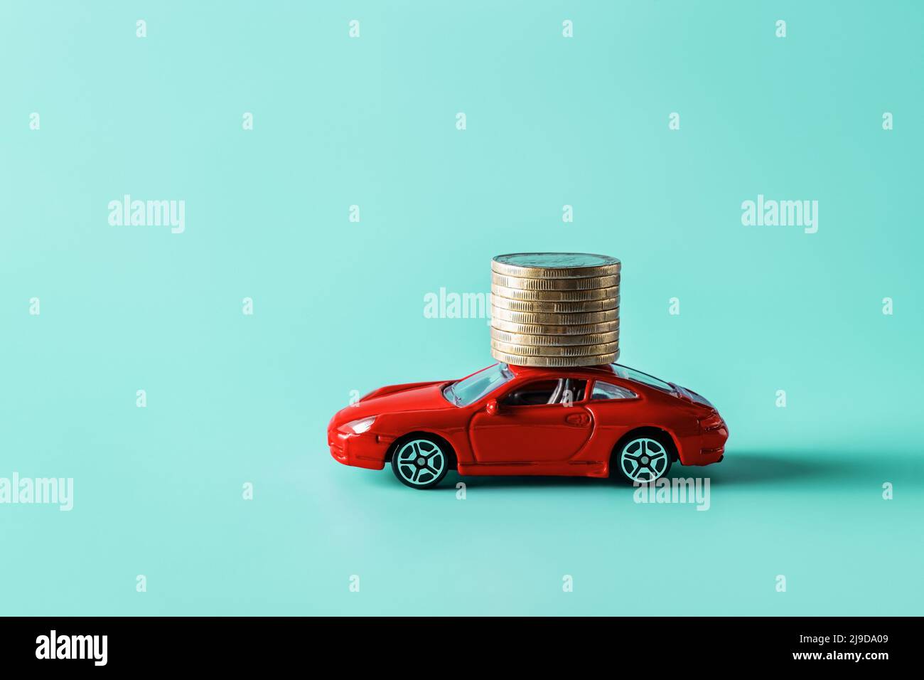 Varna, Bulgaria, 10 maggio 2022. Auto giocattolo rossa che trasporta una pila di monete su sfondo blu. Risparmio di denaro per un'auto, prestito auto, assicurazione auto. Foto Stock