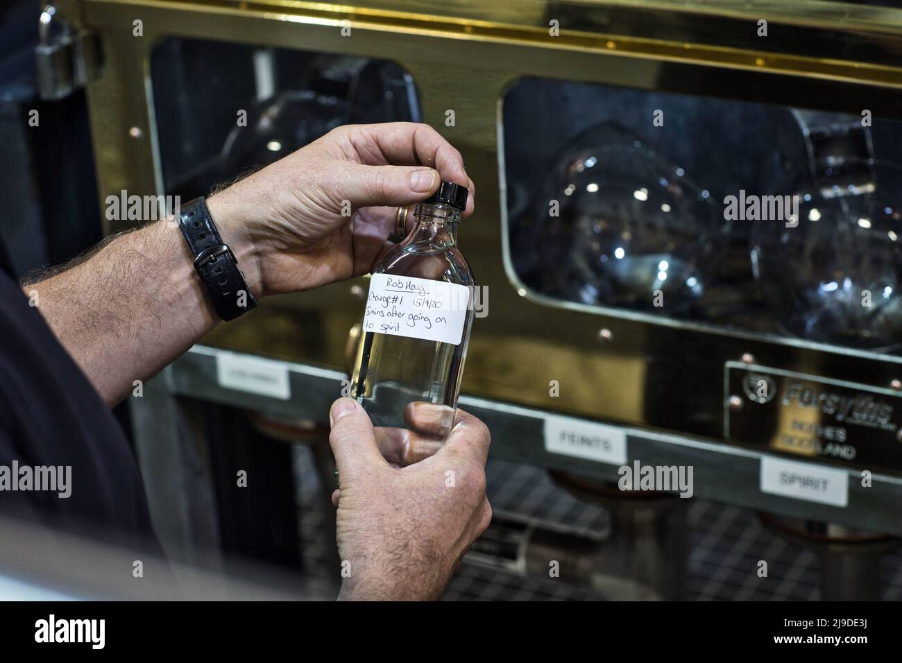 La distilleria Torabhaig sull'isola di Skye, Scozia. Still Man controlla il flacone di campione davanti a Spirit Safe. Foto Stock