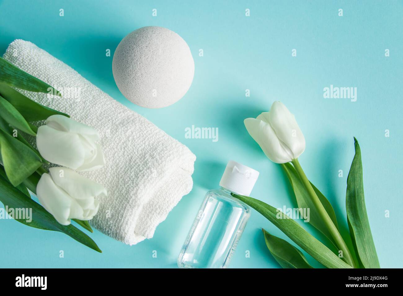 Prodotti per la cura della pelle su sfondo blu. Cosmetici naturali e tulipani bianchi. Posiziona per il testo. Foto Stock