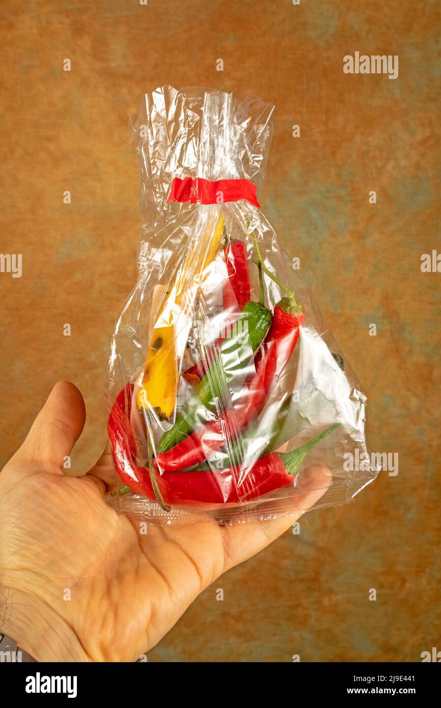 Mail mano che tiene peperoncini colorati all'interno del sacchetto di cellophane Foto Stock