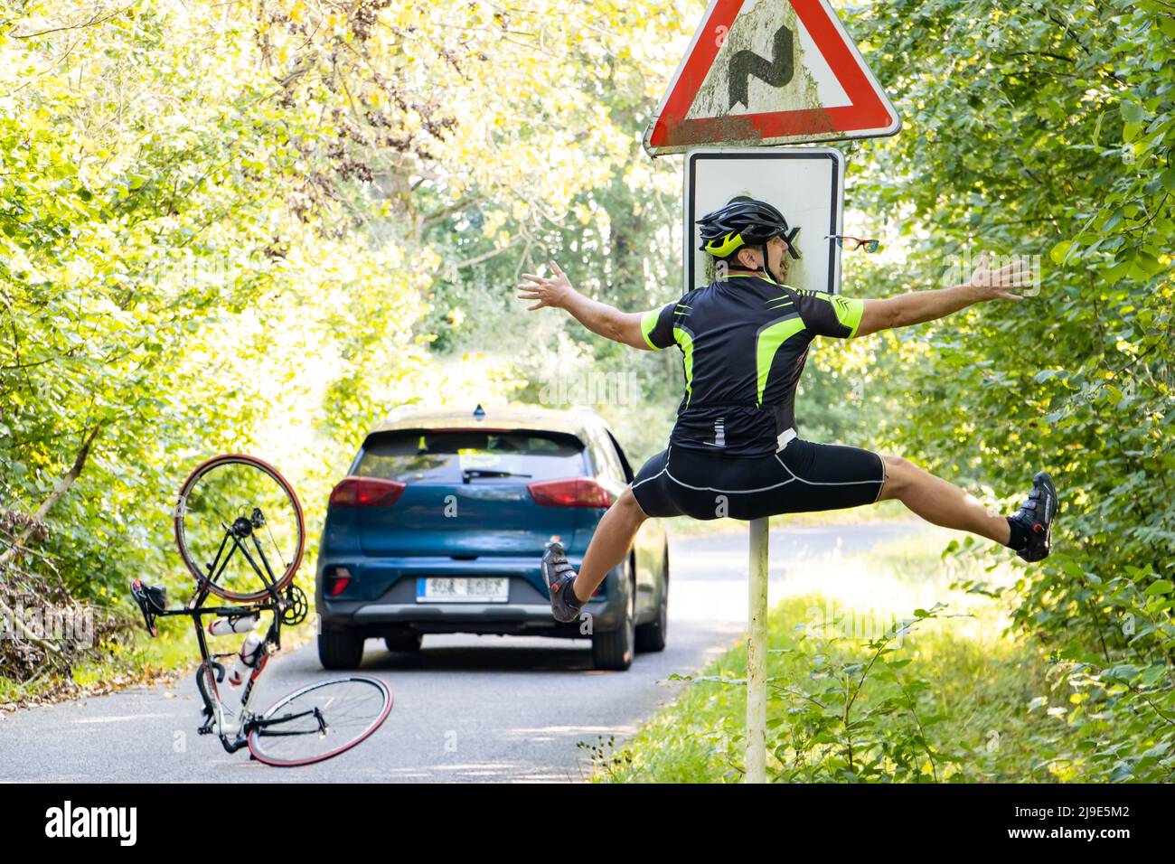 Un ciclista che cade urta in un cartello stradale accanto alla strada con traffico Foto Stock
