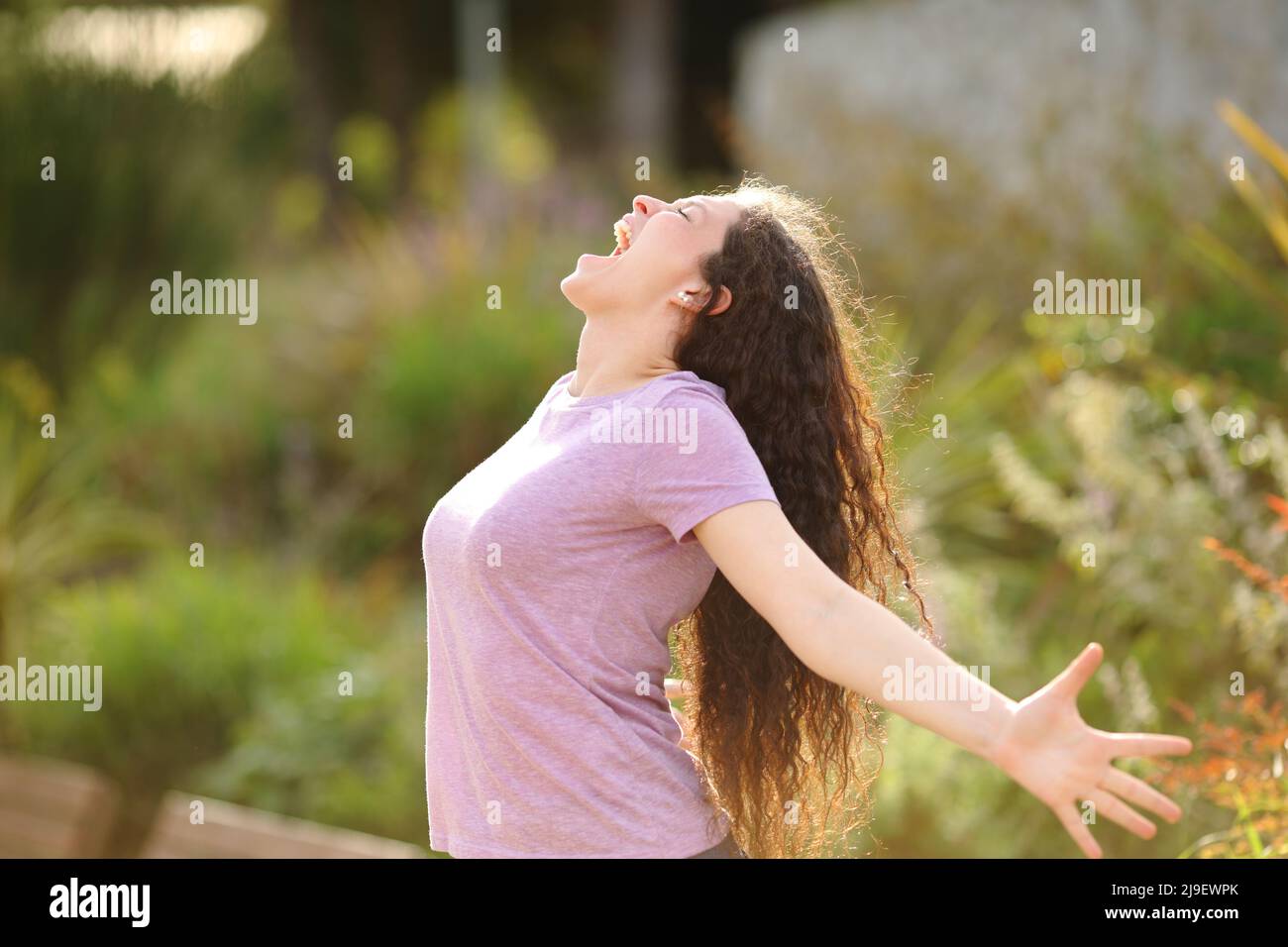 Ritratto laterale di una donna eccitata che stretching braccia e urla in un parco Foto Stock