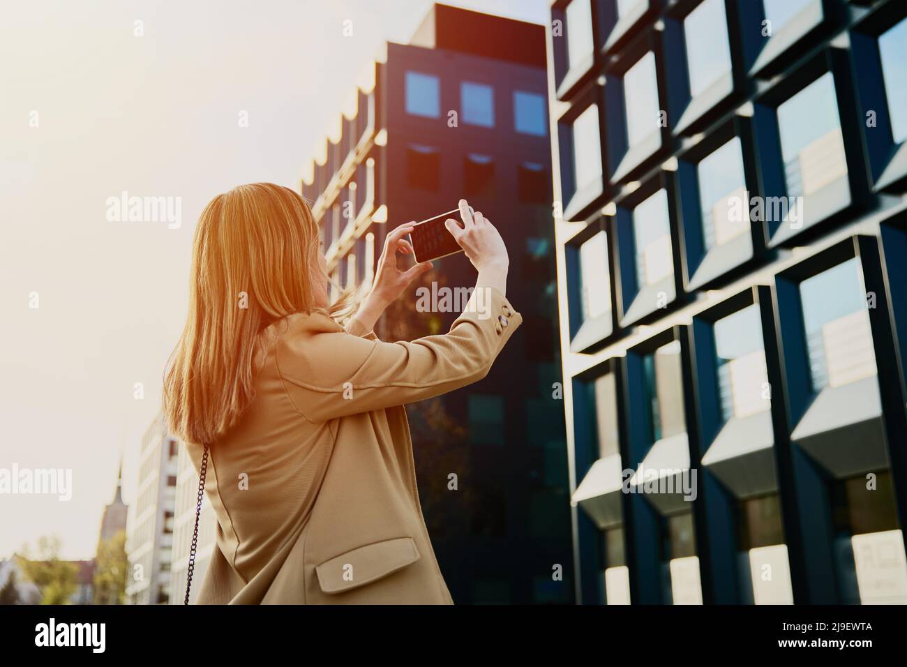 Donna caucasica millenaria godendo con giorno di sole all'aperto, scattando una foto con smartphone, turista femminile a piedi in strada città europea Foto Stock