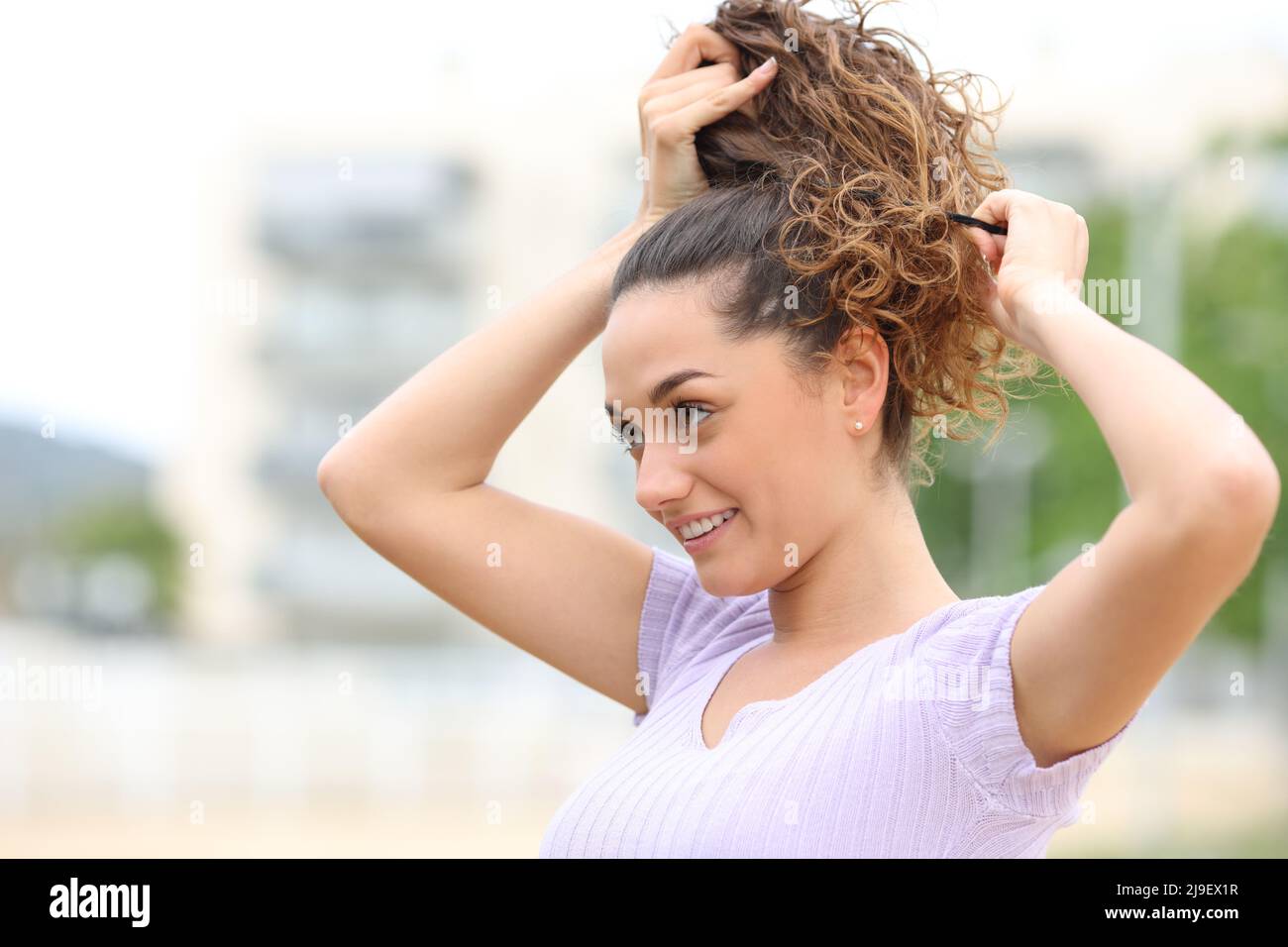 Donna felice che fa ponytail a piedi per strada Foto Stock