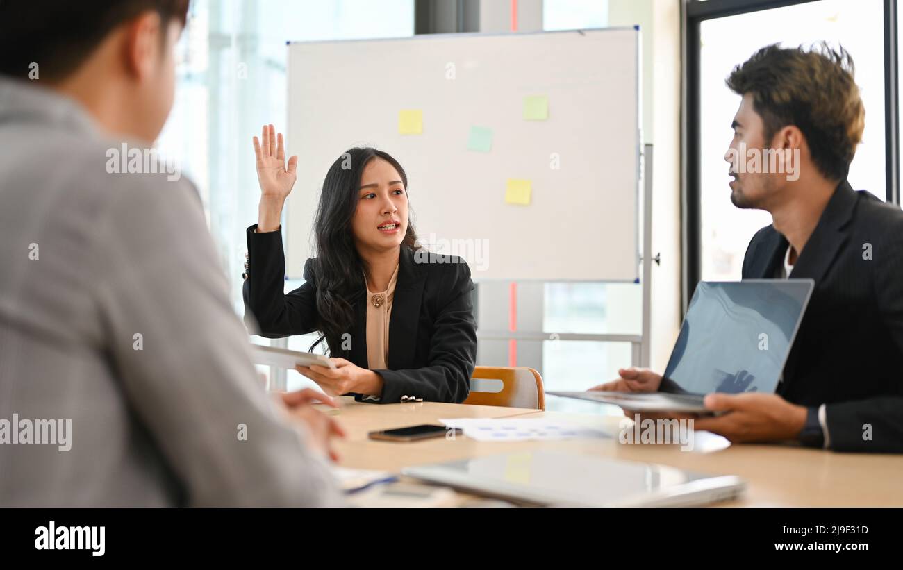 Fiduciosa donna d'affari asiatica alza la mano per condividere le sue idee nell'incontro con i colleghi. Gli uomini d'affari sono discutere e condividere le idee nel corso dell'incontro Foto Stock