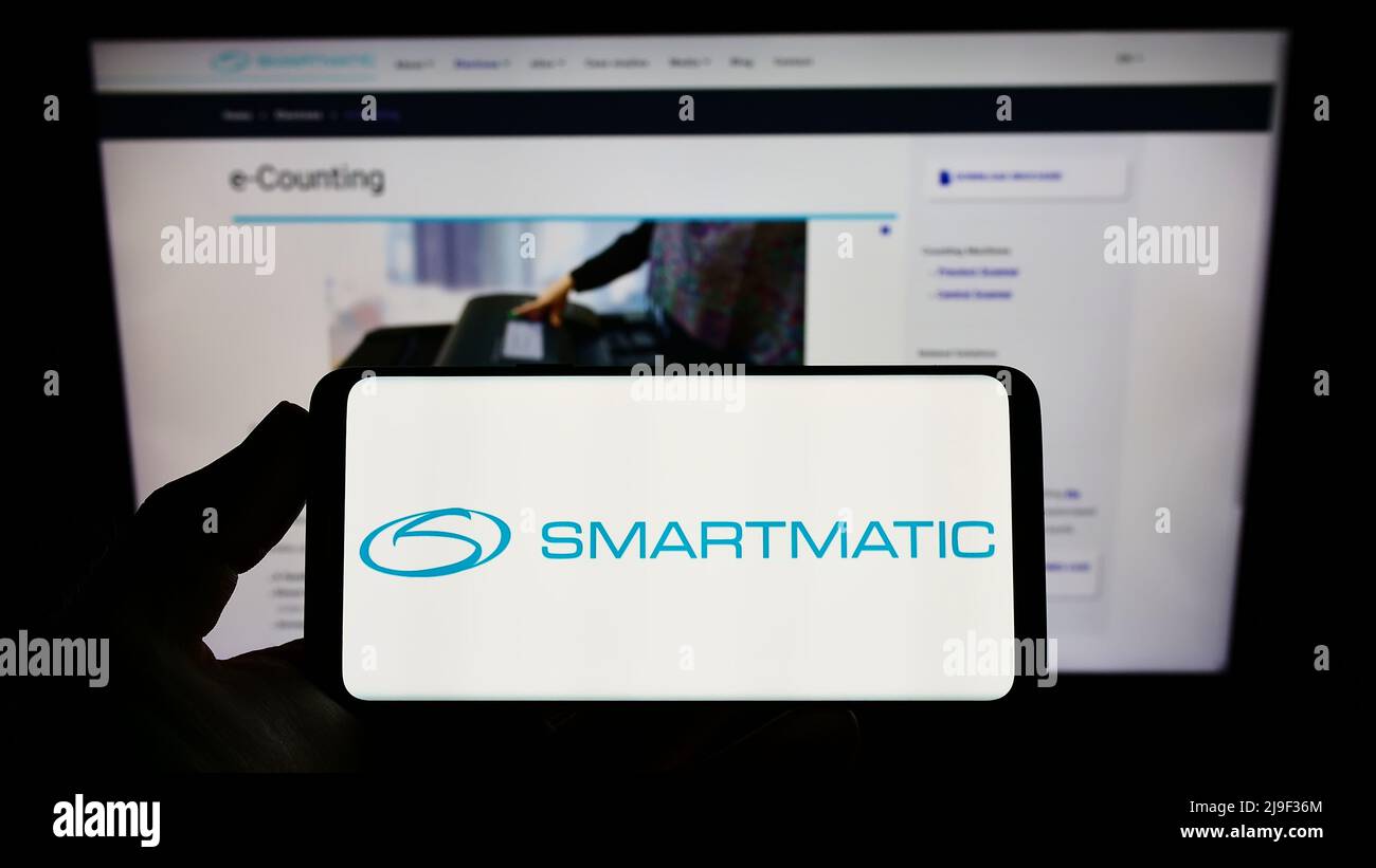 Persona che tiene smartphone con logo della società del sistema di voto Smartmatic Corporation sullo schermo di fronte al sito web. Mettere a fuoco sul display del telefono. Foto Stock