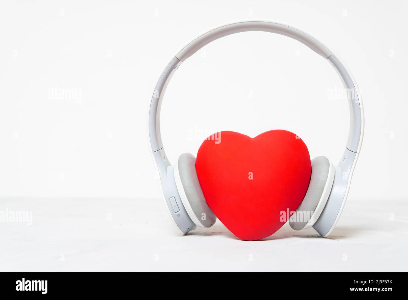 Cuffie wireless con un grande cuore rosso isolato su sfondo neutro con spazio di copia. Ascolta il tuo cuore concetto. Foto Stock