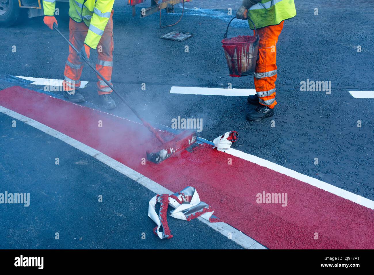I lavoratori della strada che applicano la vernice di marcatura rossa calda sulla strada di costruzione nuova Foto Stock