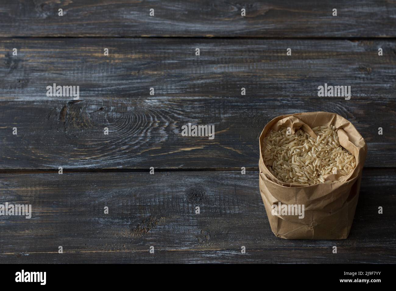 Riso bruno crudo a grana lunga in un sacco di carta artigianale su uno sfondo di legno, spazio Foto Stock