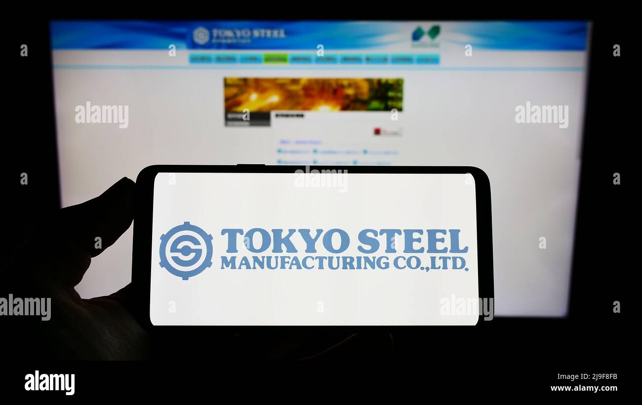 Persona che tiene il telefono mobile con il logo della società giapponese Tokyo Steel Co. Ltd sullo schermo di fronte al Web page di affari. Mettere a fuoco sul display del telefono. Foto Stock