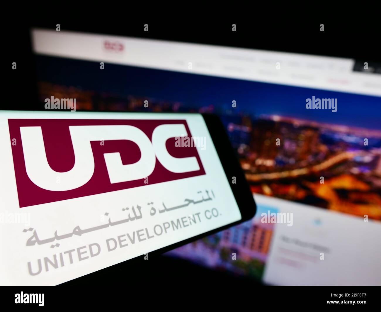 Smartphone con logo di United Development Company Q.P.C. (UDC) sullo schermo di fronte al sito Web aziendale. Mettere a fuoco sulla sinistra del display del telefono. Foto Stock