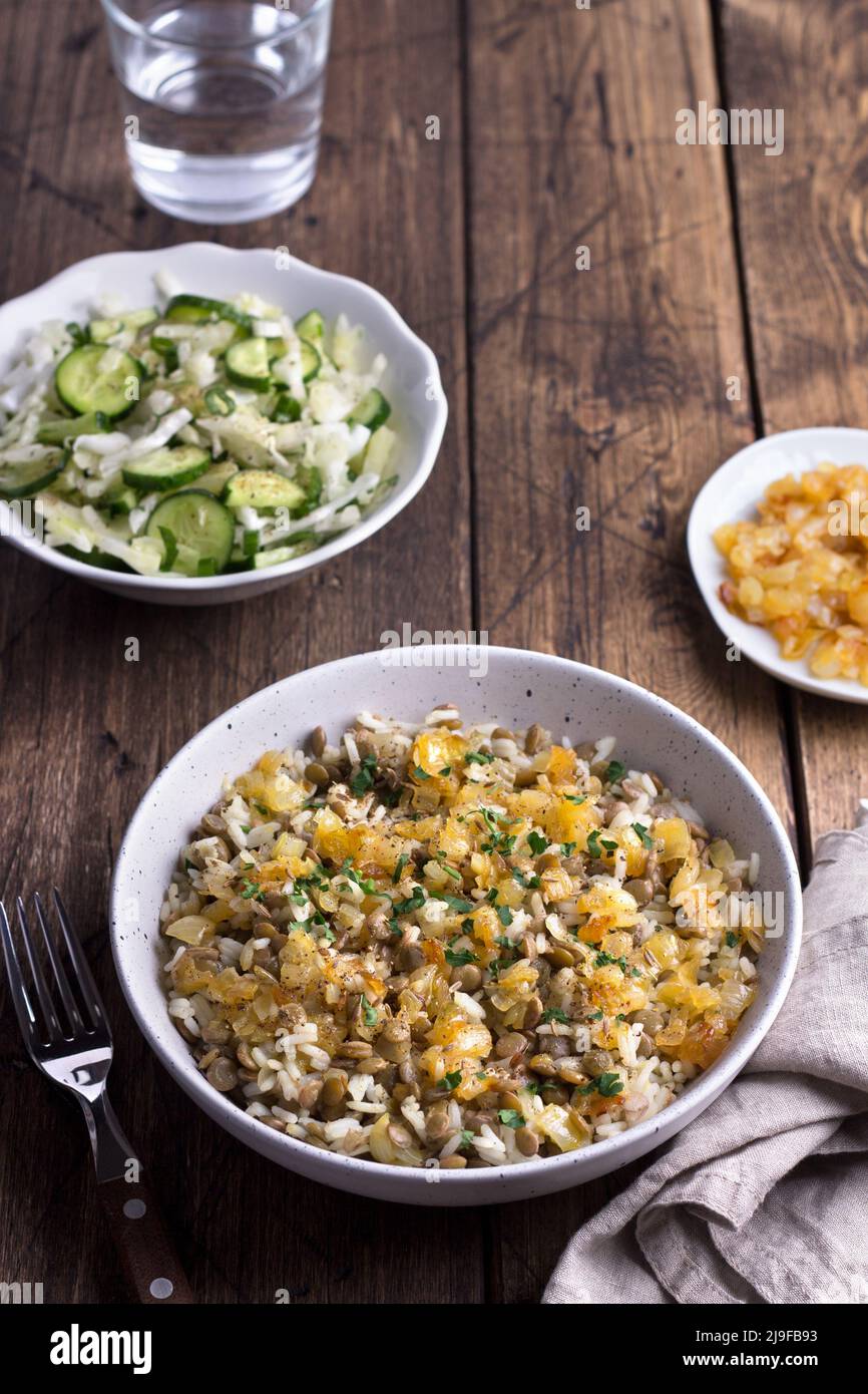 Piatto tradizionale mediorientale, Mujadara di lenticchie, riso e cipolle fritte con un'insalata di cavolo e cetrioli su tavola di legno, vista dall'alto, spazio, se Foto Stock