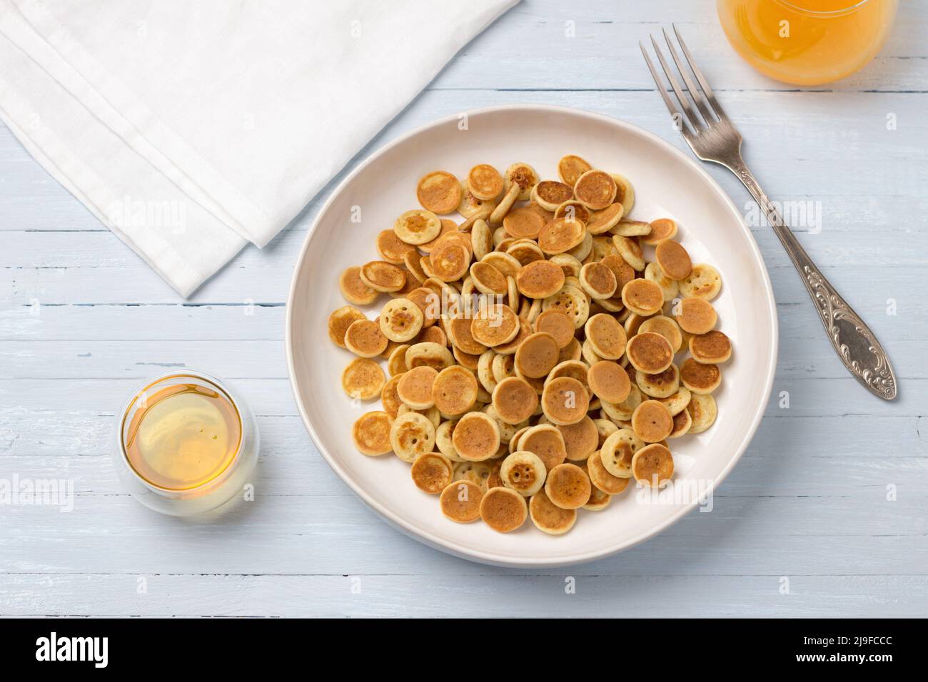 Piatto di mini pancake con cereali con miele e succo d'arancia fresco su sfondo blu chiaro. Cibo alla moda. Colazione fatta in casa. Vista dall'alto Foto Stock