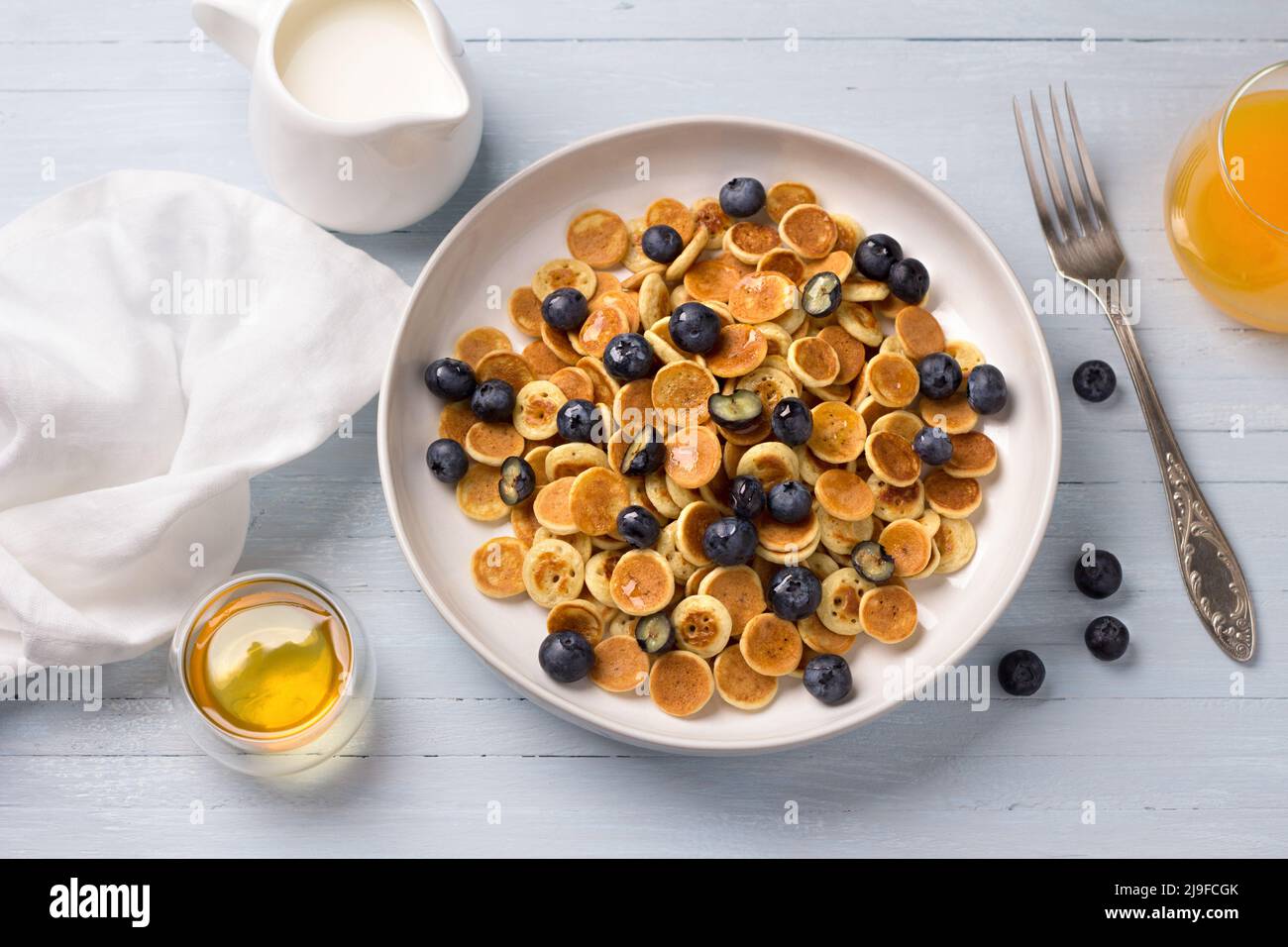 Piatto di mini pancake cereali con miele, bacche, panna e succo d'arancia fresco su sfondo azzurro. Cibo alla moda. Colazione fatta in casa. Vista dall'alto Foto Stock