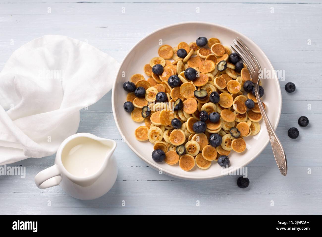 Piatto di mini pancake con cereali con crema, miele e frutti di bosco su sfondo blu chiaro. Cibo alla moda. Colazione fatta in casa. Vista dall'alto Foto Stock