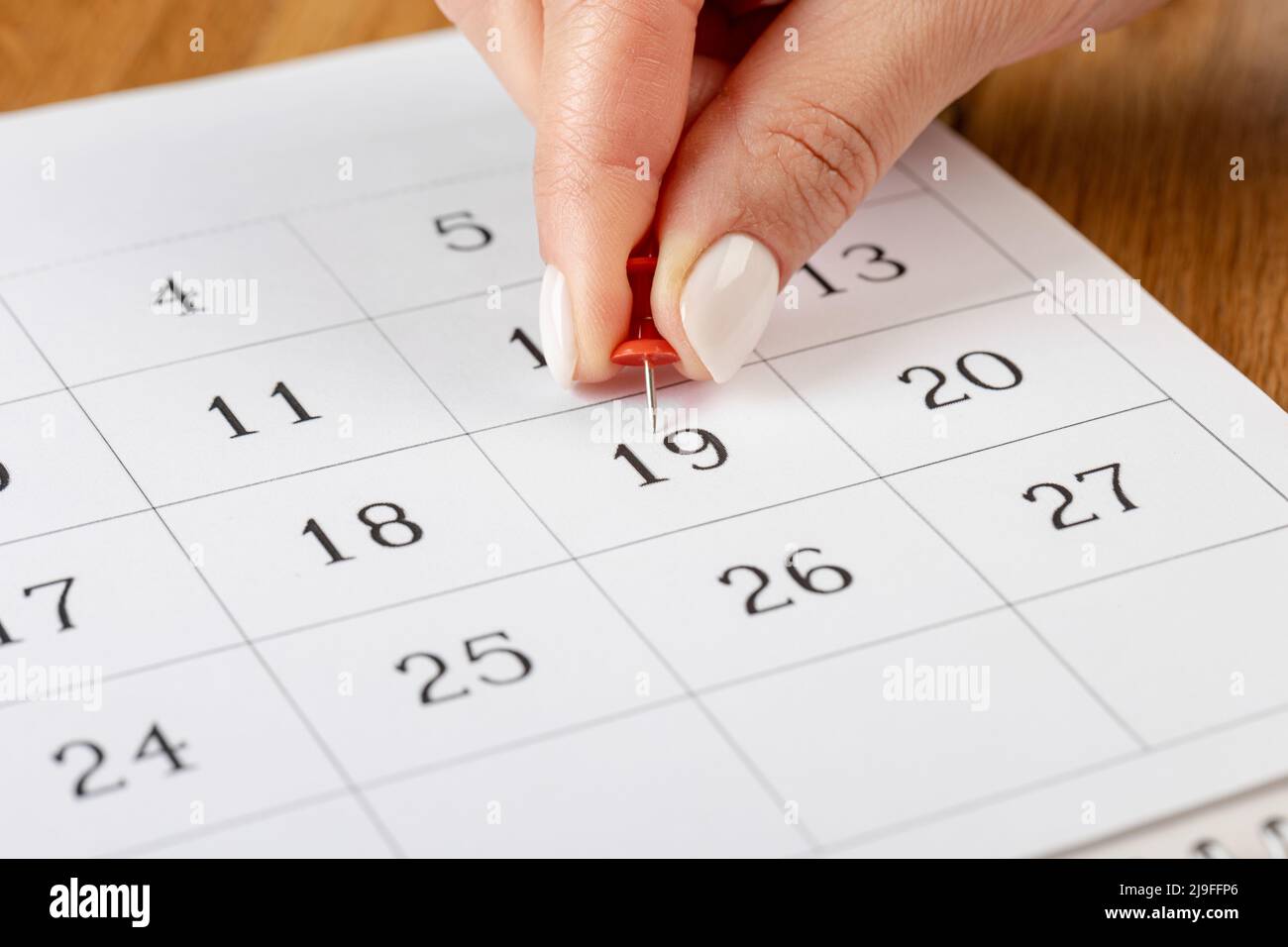 Pin a mano rosso bloccato il giorno del mese nel calendario, business concept. Belle dita a mano femminile Foto Stock