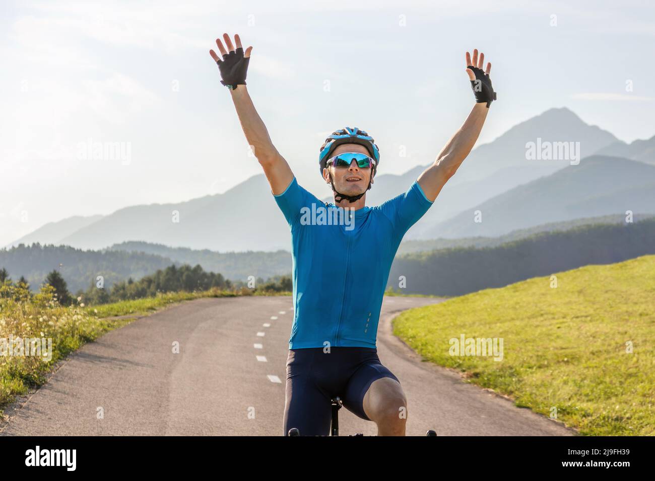 Atleta maschile professionista da corsa in bicicletta con le braccia sollevate sopra la testa, in una posizione di vittoria Foto Stock