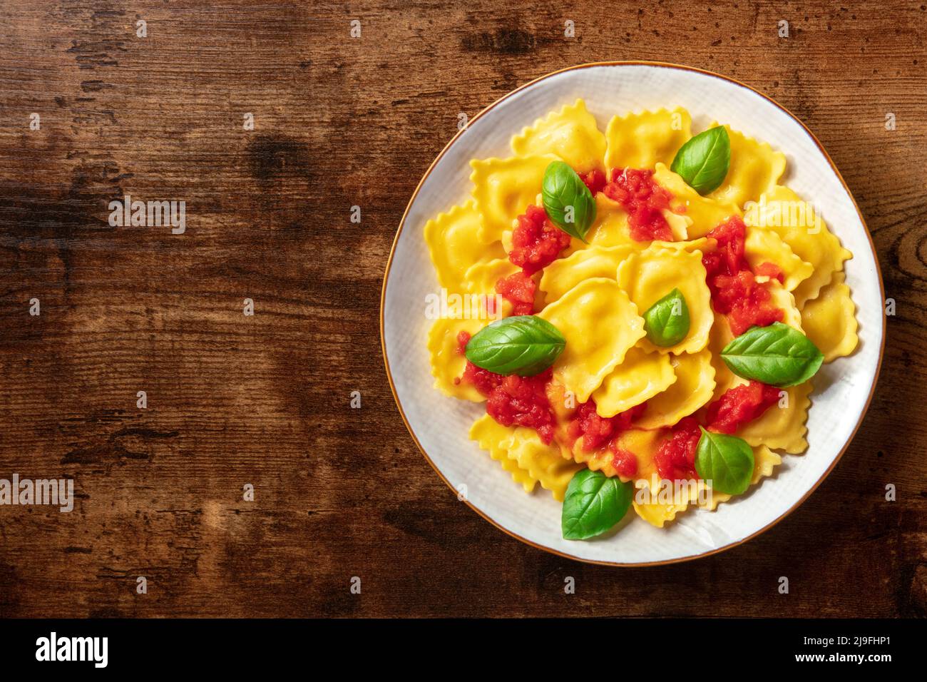 Ravioli con salsa di pomodoro e basilico. Un piatto di pasta farcita, sparato dall'alto, cena vegetariana su sfondo rustico scuro in legno con spazio copia Foto Stock