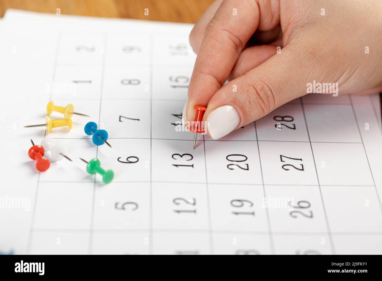 Pin a mano rosso bloccato il giorno del mese nel calendario, business concept. Belle dita a mano femminile Foto Stock
