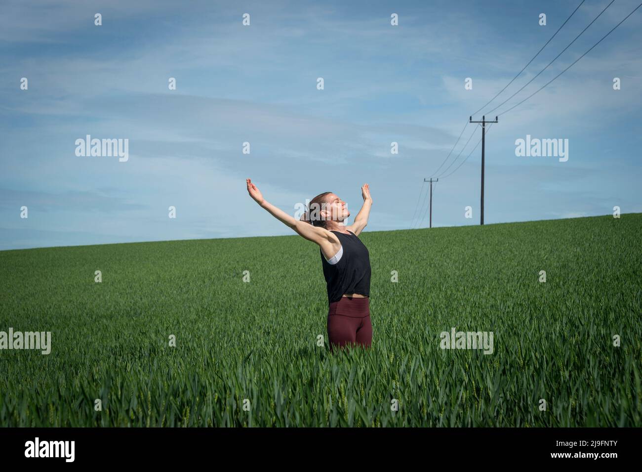 Donna in piedi in un campo di grano con le braccia alzate e godere del sole Foto Stock