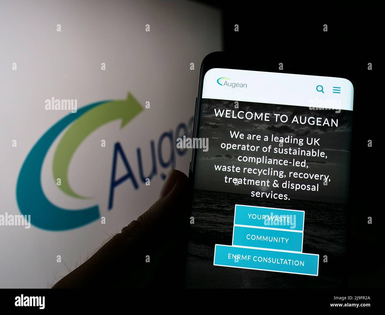 Persona che tiene smartphone con sito web della società britannica di gestione dei rifiuti Augean plc sullo schermo con logo. Concentrarsi sul centro del display del telefono. Foto Stock