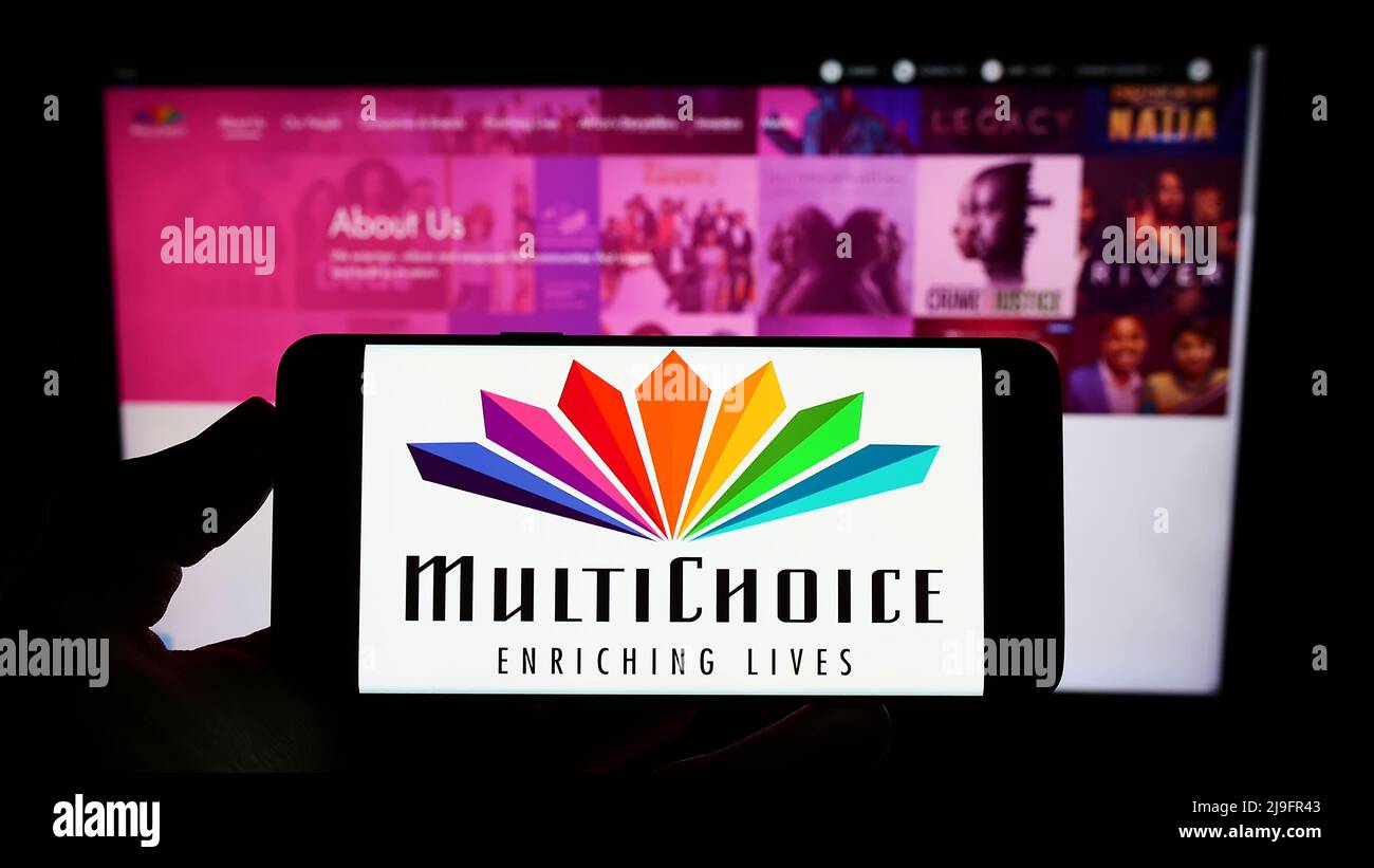 Persona che tiene sullo schermo uno smartphone con il logo della società di media sudafricana Multichoice Group di fronte al sito Web. Mettere a fuoco sul display del telefono. Foto Stock