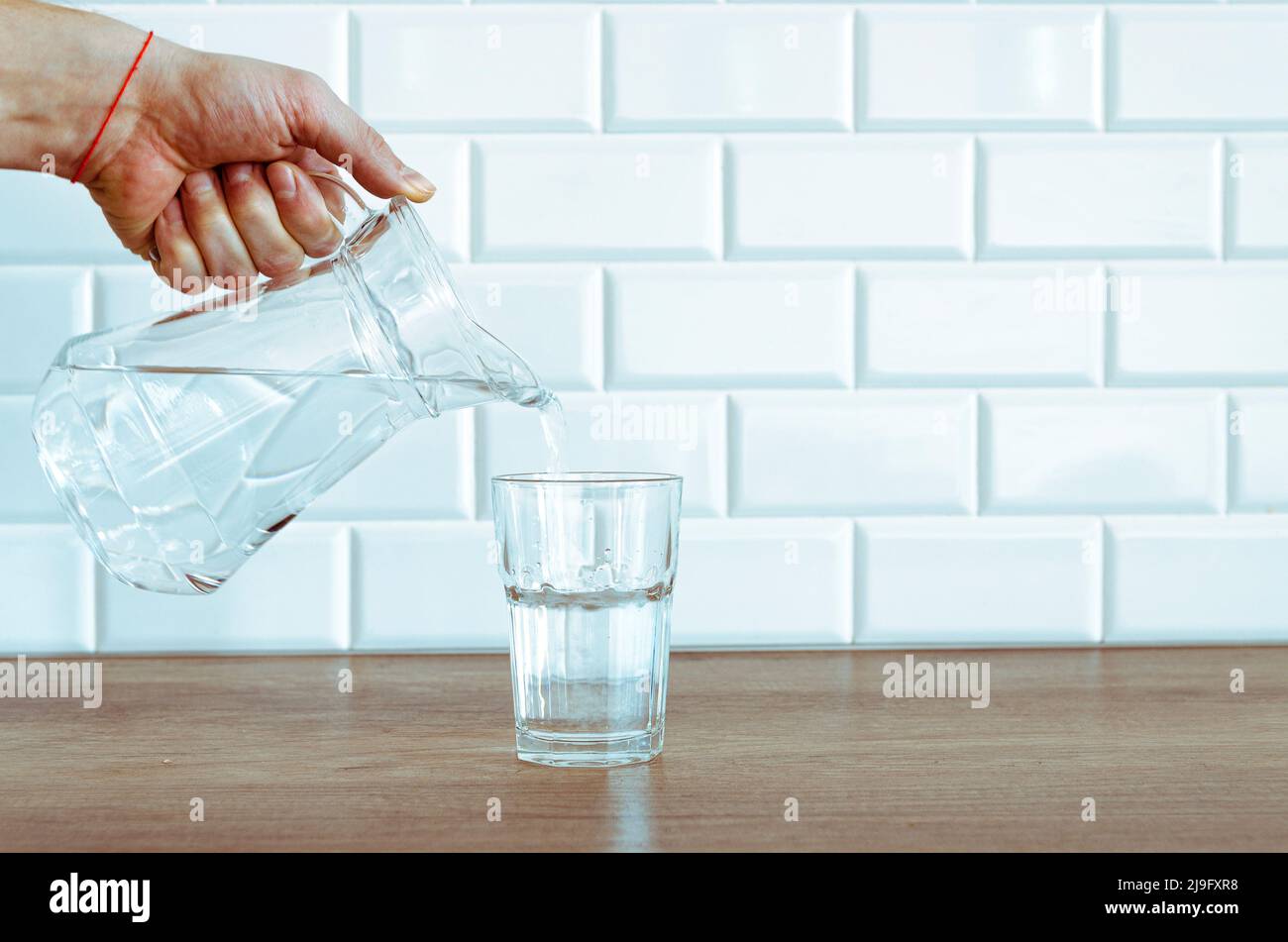 Versando acqua fresca purificata dalla caraffa in vetro sul tavolo Foto Stock