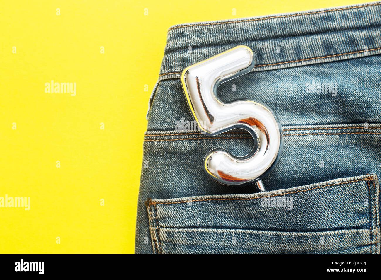 numero 5 che sporge dalla tasca posteriore di jeans blu su sfondo giallo Foto Stock