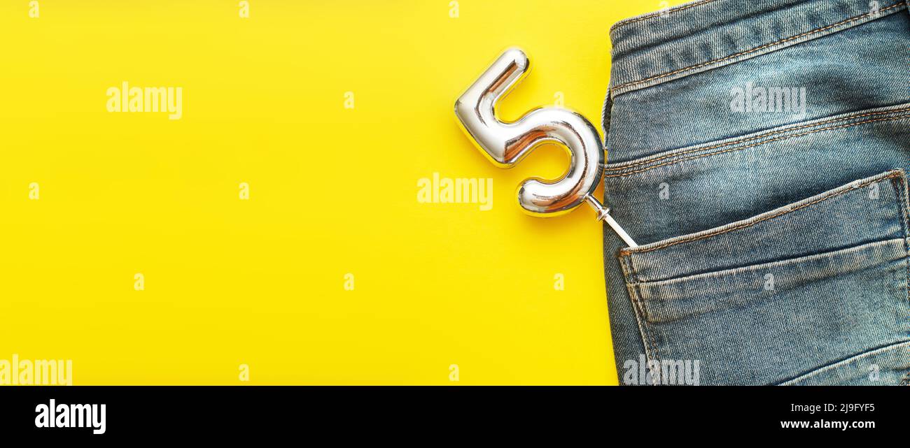 numero 5 che sporge dalla tasca posteriore di jeans blu su sfondo giallo Foto Stock