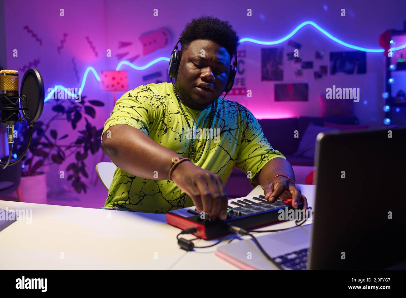 Ritratto del giovane musicista Z Black indossando le cuffie seduti alla scrivania a casa lavorando su una traccia audio utilizzando sintetizzatore e computer portatile Foto Stock
