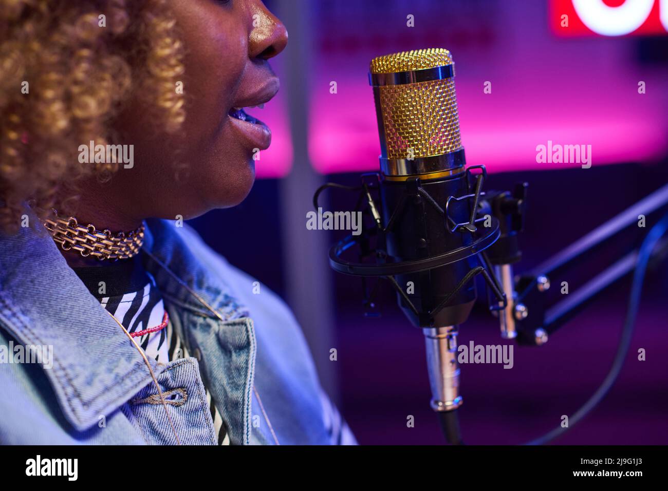 Vista laterale primo piano della giovane donna nera seduta di fronte al microfono che registra podcast o fa trasmissioni radio Foto Stock