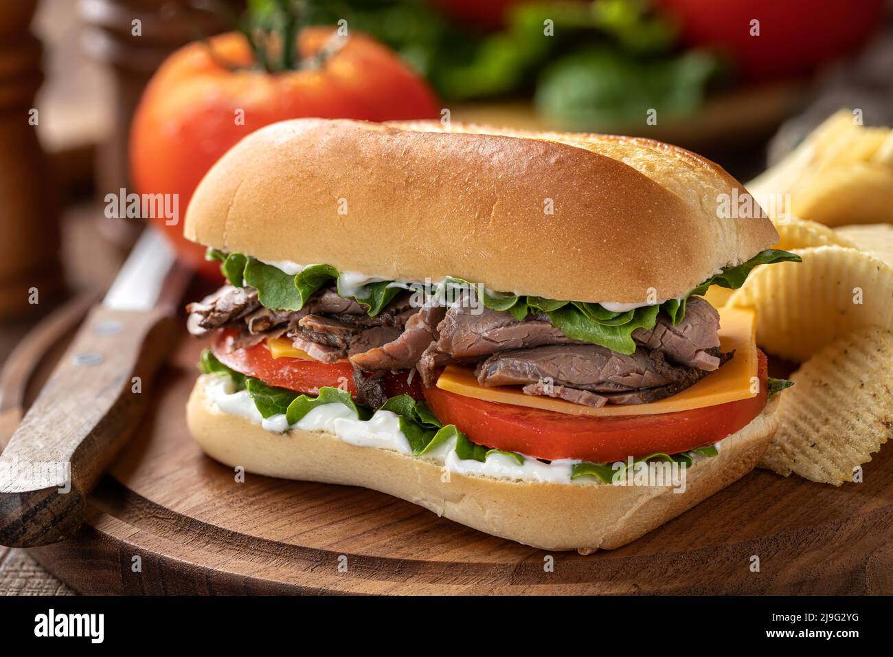 Sandwich di manzo arrosto con formaggio, pomodoro e lattuga su un tagliere di legno Foto Stock