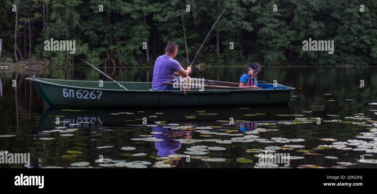 Padre e figlio che pescano sul lago rurale al tramonto su una barca. Banner Foto Stock