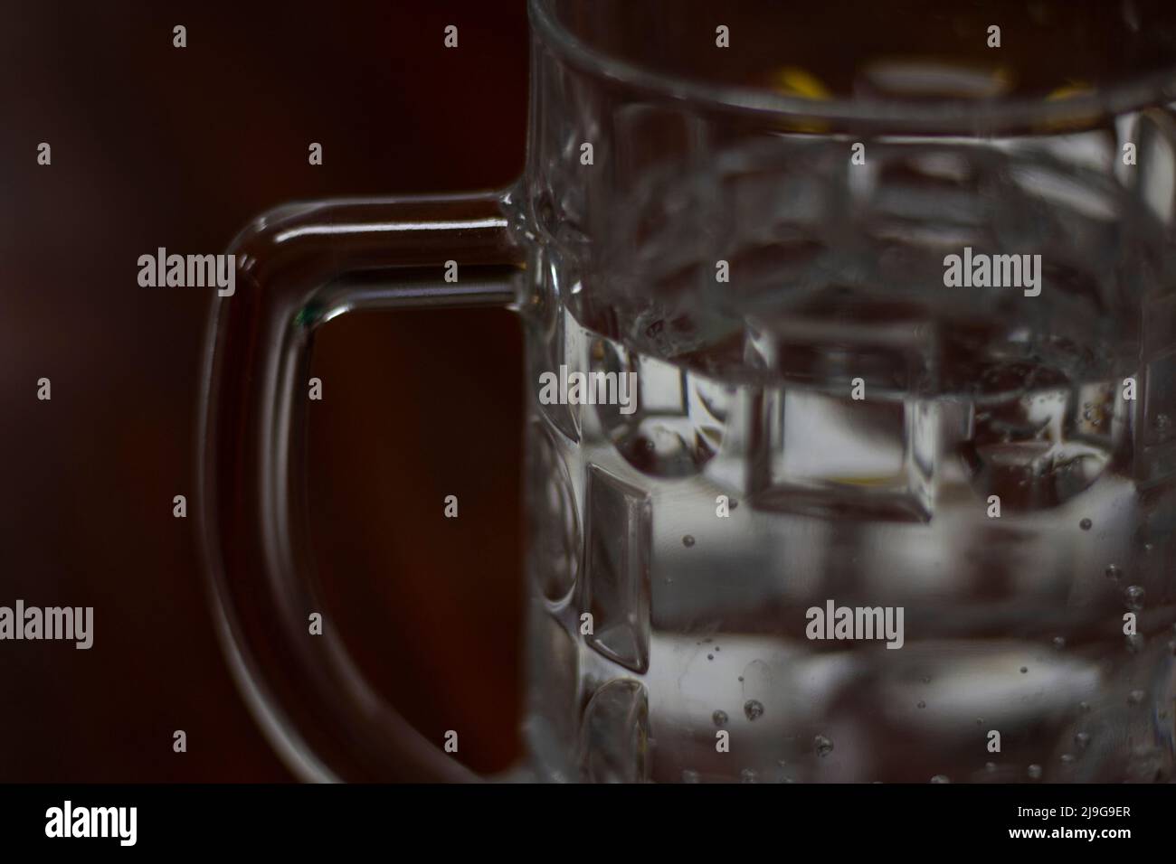 Dettagli vetro. Tazza di acqua. Lo sfondo è di vetro spesso. L'acqua fresca viene versata nella tazza. Foto Stock
