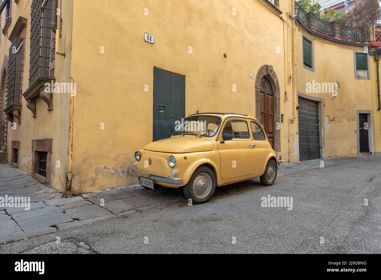 Auto classica Fiat 500 d'epoca gialla contro il muro giallo nella stretta strada medievale centro storico di Lucca Foto Stock