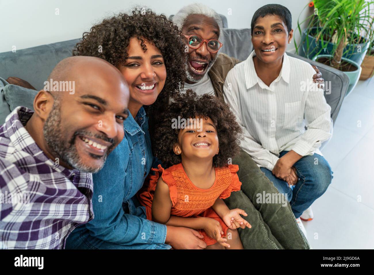 Happy family sitting on sofa while taking selfie Foto Stock