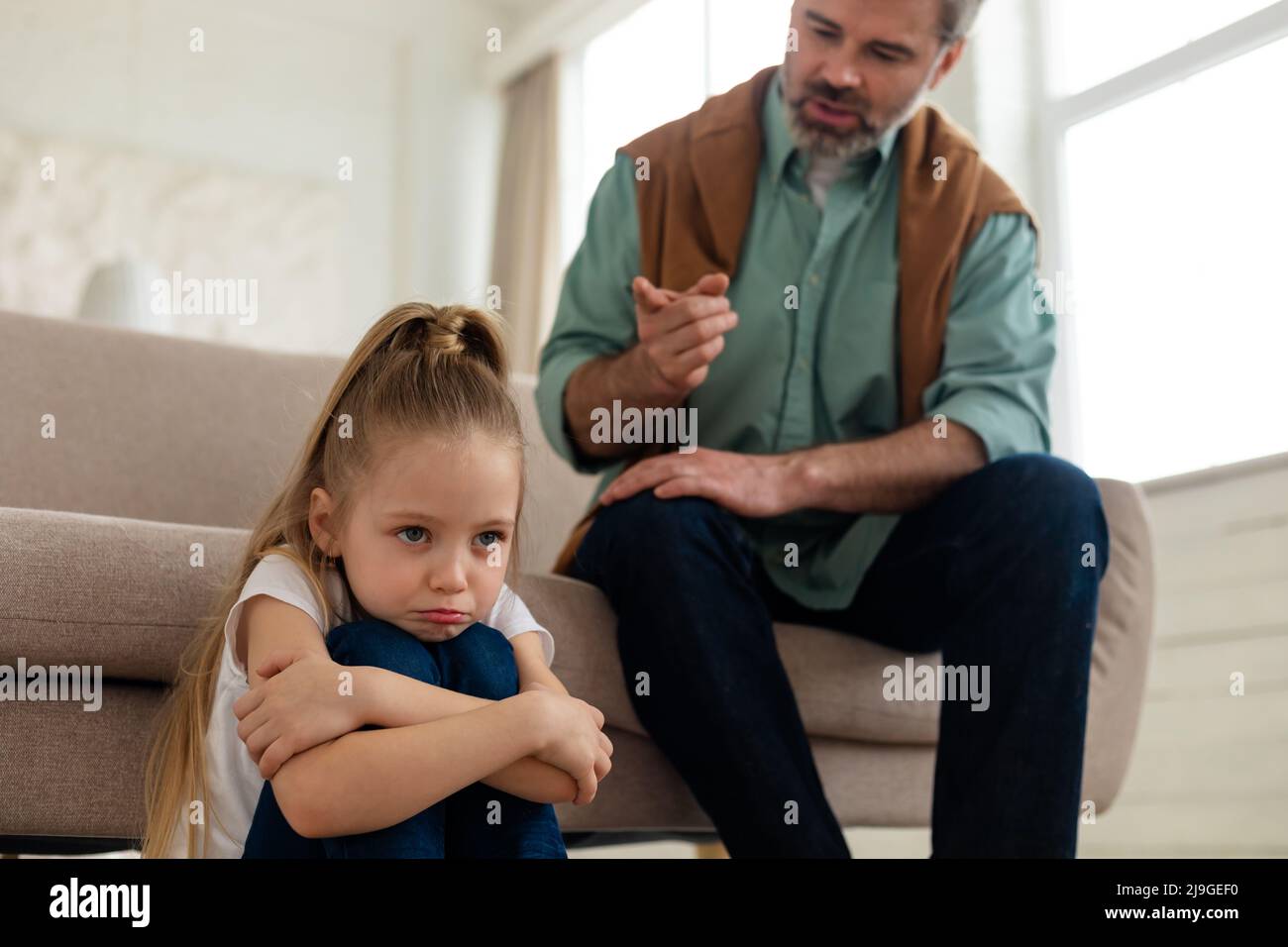 Padre severo che scolding la figlia triste piccola seduta a casa Foto Stock