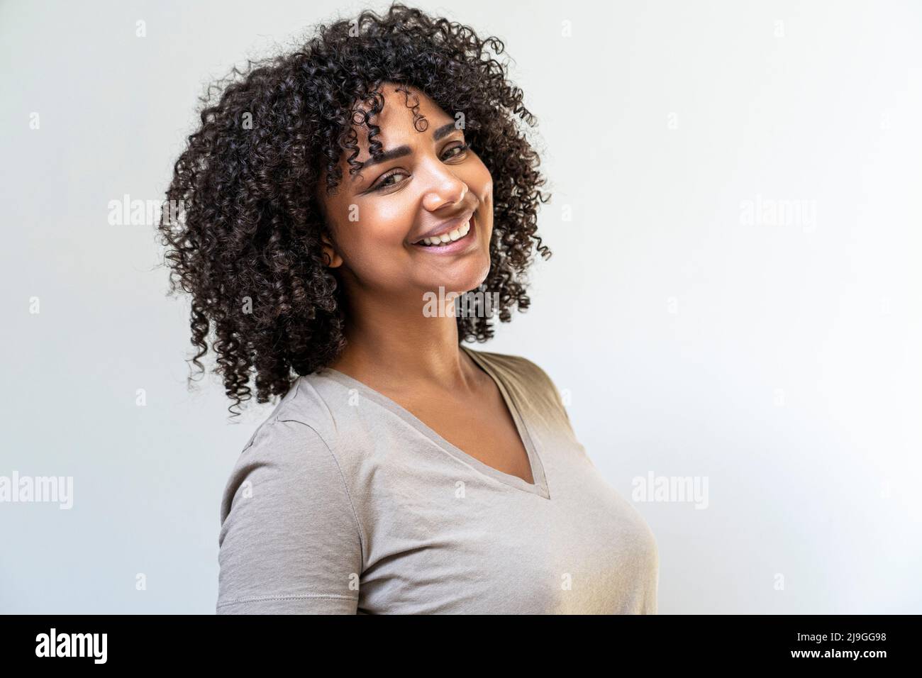 Donna sorridente in piedi contro il muro bianco Foto Stock