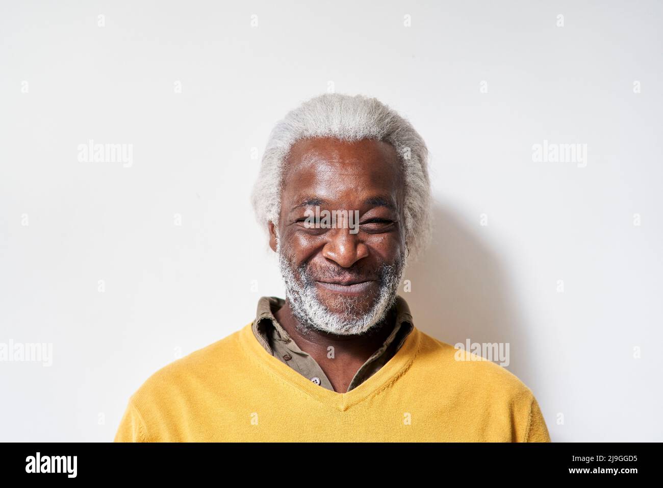 Uomo anziano sorridente in piedi contro il muro Foto Stock