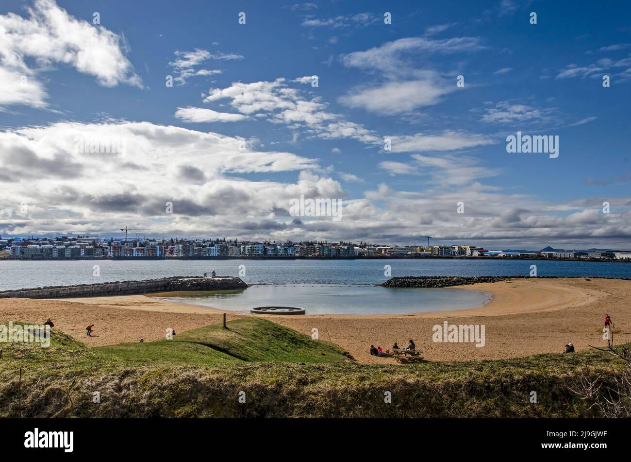 Reykjavik, Islanda, 21 aprile 2022: Spiaggia di sabbia a Nautholsvik sotto un cielo soleggiato con quartieri suburbani sul lato opposto della baia Foto Stock
