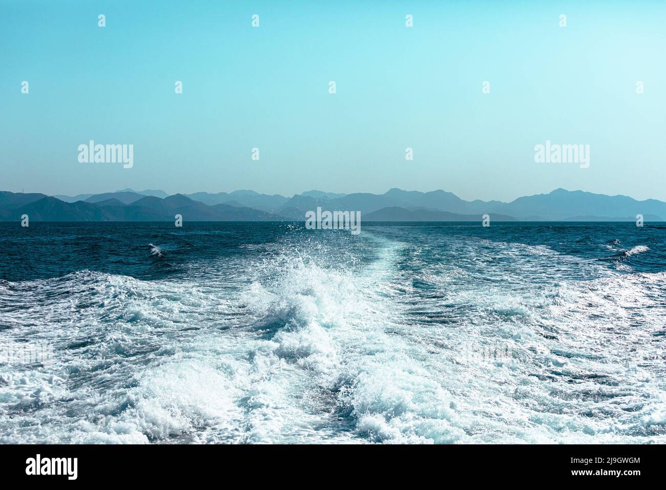 Vista da una nave ad alta velocità sul mare blu con una costa montagnosa sullo sfondo Foto Stock