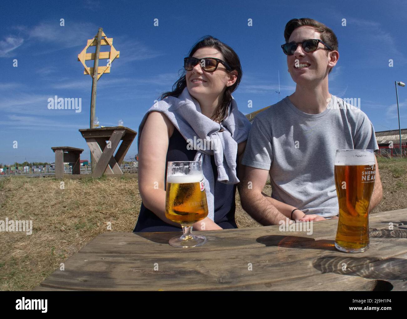 Giovane coppia che si gode un drink su una panchina soleggiata da pub, guardando in lontananza. Fotografia di un uomo e una donna con uno stile di vita luminoso e rilassato Foto Stock
