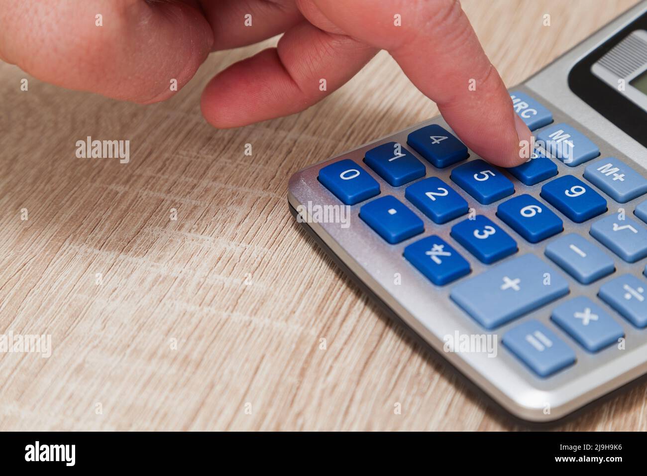 Primo piano della mano di una persona premendo il tasto numero otto sulla tastiera di una calcolatrice grigia con pulsanti blu su un tavolo di legno. Foto Stock