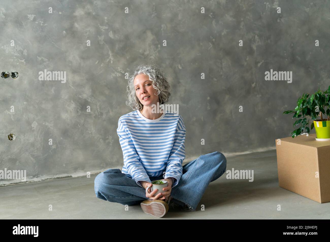 Donna con tazza da tè seduta a terra davanti al muro Foto Stock