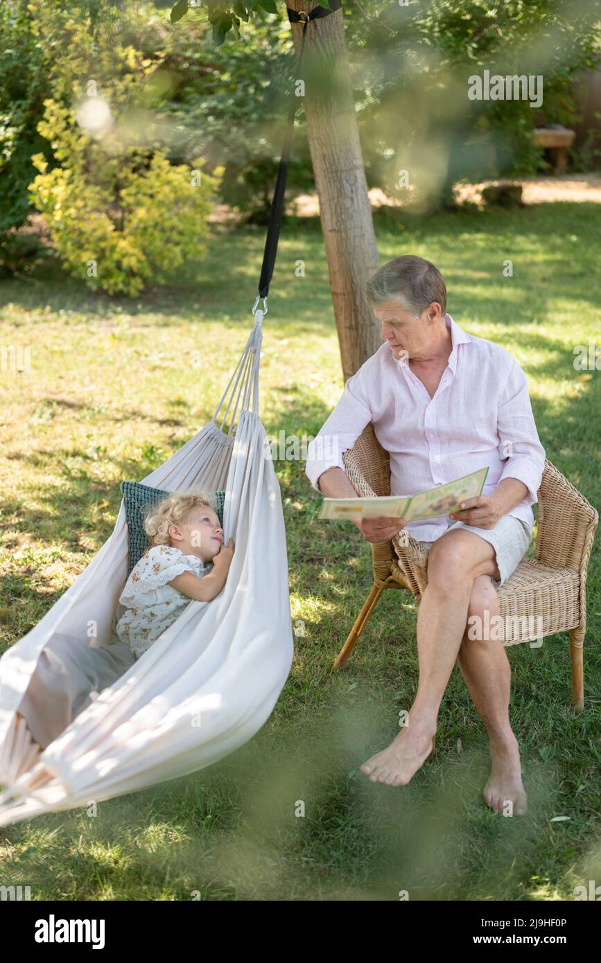 Nonno che legge la storia alla nonna che giace in amaca in giardino Foto  stock - Alamy
