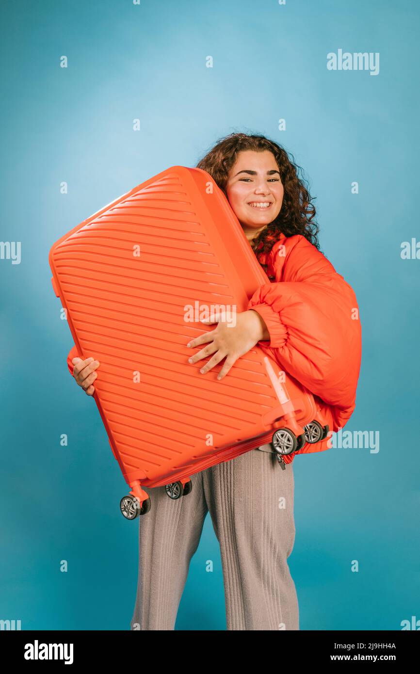 Felice giovane donna che porta la valigia arancione su sfondo blu Foto Stock