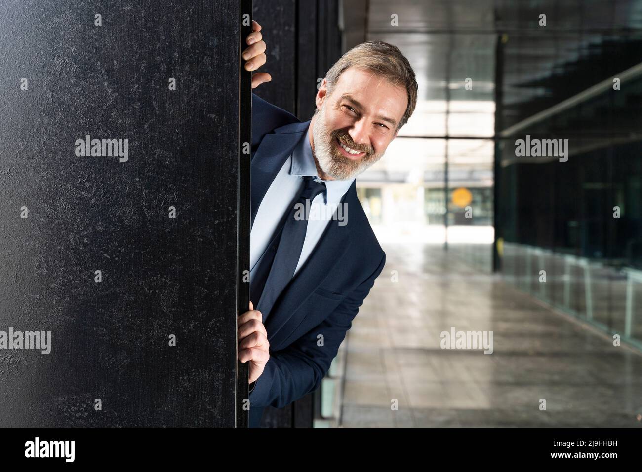 Un uomo d'affari felice che sbirca da dietro la colonna nera Foto Stock