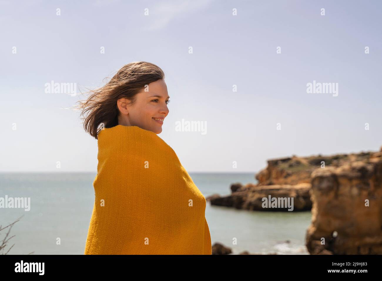 Donna felice avvolto in coperta gialla godendo giorno di sole Foto Stock