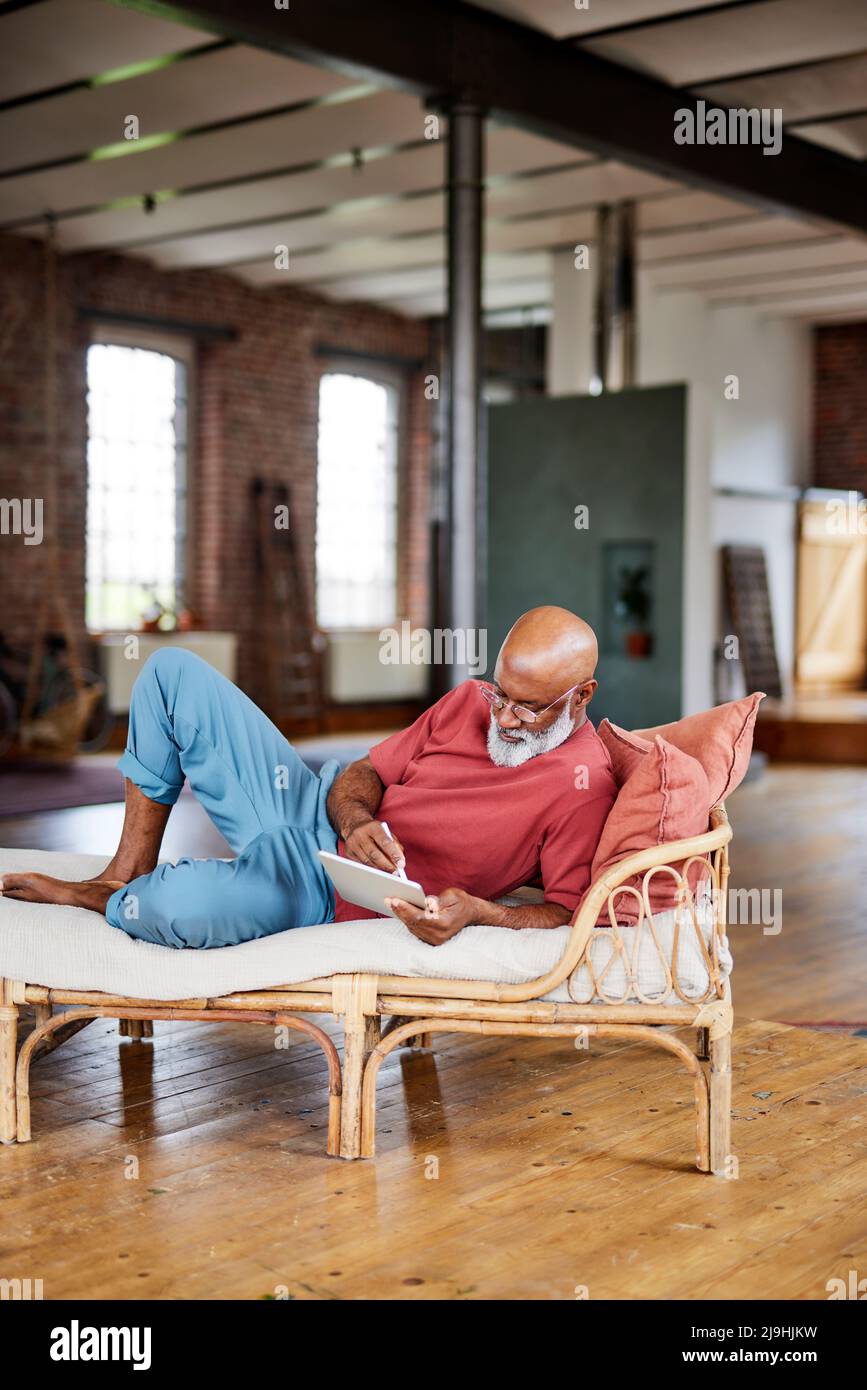 Uomo maturo che usa un tablet PC sul divano di casa Foto Stock
