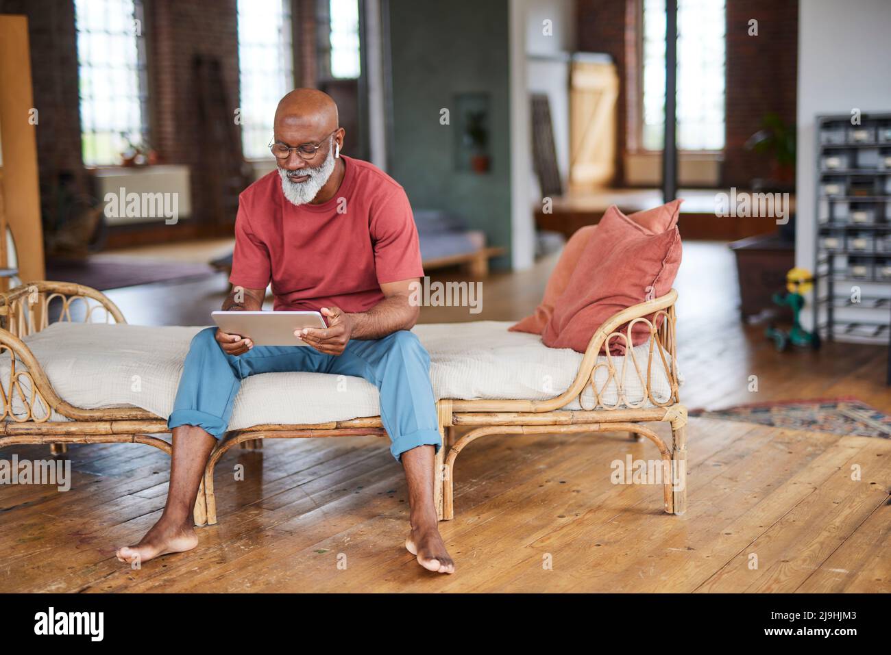 Uomo calvo che usa un tablet PC seduto sul divano di casa Foto Stock